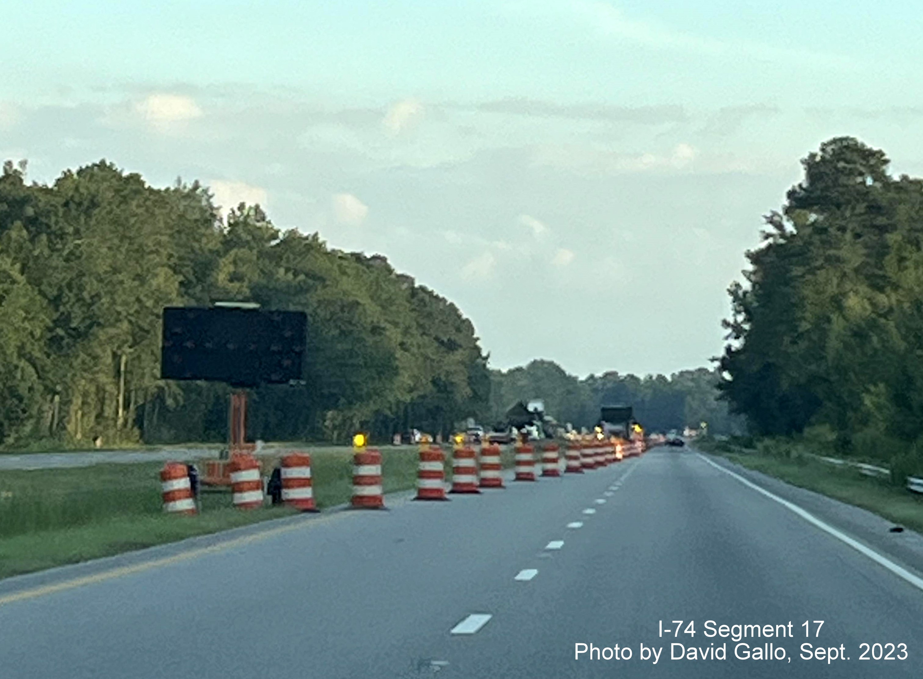 Image of construction barrels marking beginning of left lane closure approaching the NC 72 intersection on 
         US 74 West in interchange project work zone, David Gallo, September 2023