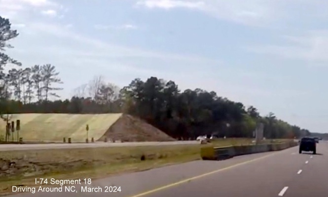 Image of fill piled up for future Old Lake Road bridge over US 74/76 (Future I-74) in Lake Waccamaw 
       construction zone, screen shot from video by Driving Around NC, April 2024