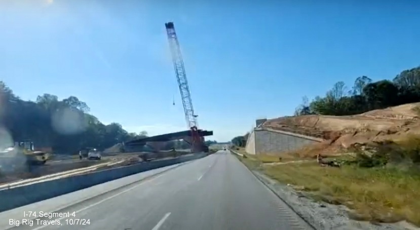 Image of partially completed flyover ramp over I-74 West that will carry eastbound traffic
        to the Winston-Salem Northern Beltway, screen grab of Big Rig Travels video, October 2024