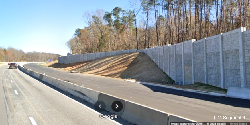 Image of paved future eastbound lanes and the completed noise wall beyond 
	  site of the future Winston-Salem Northern Beltway interchange on I-74 East, Google Maps Street View, March 2025