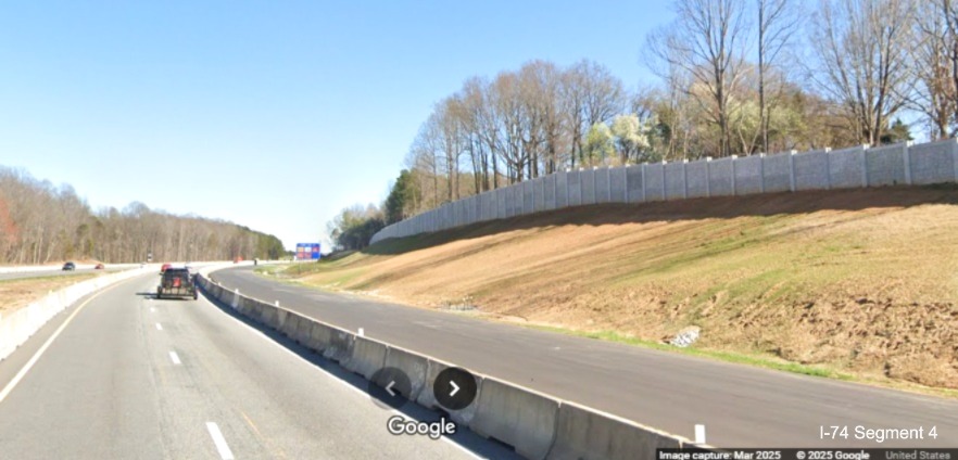 Image of paved future eastbound lanes and the completed noise wall heading towards 
	  the Union Cross Road interchange on I-74 East, Google Maps Street View, March 2025
