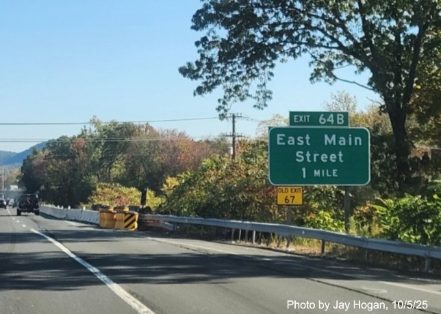 Image of ground mounted 1 Mile advance sign for the East Main Street exit, with
 new milepost based exit number overlay on exit tab and yellow Old Exit 67 sign on support post on CT 15 North/Cross Parkway 
 in Meriden, by Jay Hogan, August 2025