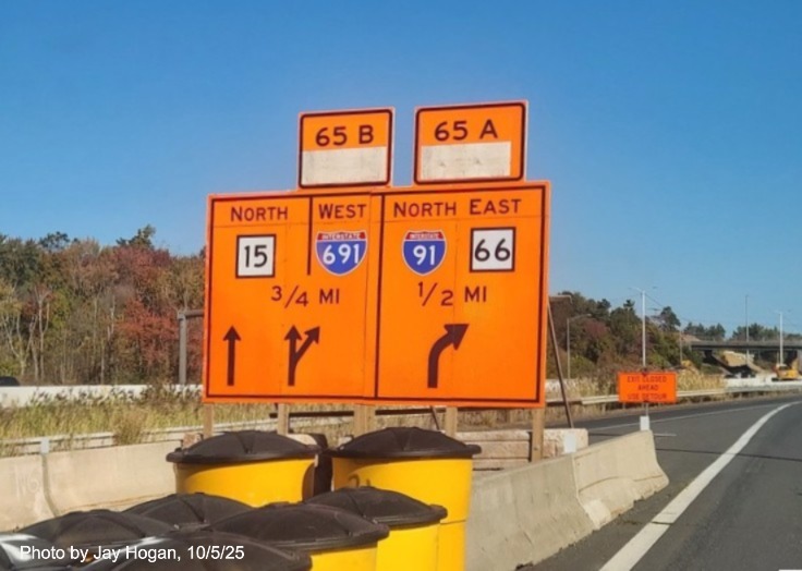 Image of temporary orange ground mounted exit sign for the I-91 exits, with
 new milepost based exit number exit tabs on CT 15 North/Cross Parkway in Meriden, by Jay Hogan, August 2025