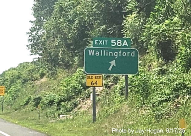 Image of ground mounted ramp sign for the Wallingford exit, with
 new milepost based exit number overlay on exit tab and Old Exit 64 sign on support post on CT 15 South/Cross Parkway 
 in Wallingford, by Jay Hogan, August 2025