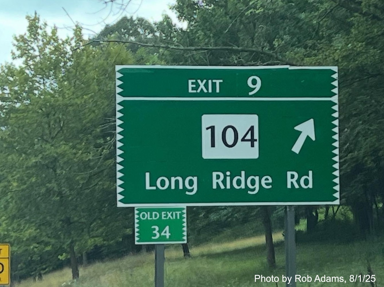 Image of ground mounted ramp sign for the CT 104 exit, with new milepost based exit number 
 and small Old Exit 34 sign attached to support post on CT 15 North/Merritt Parkway in Stamford