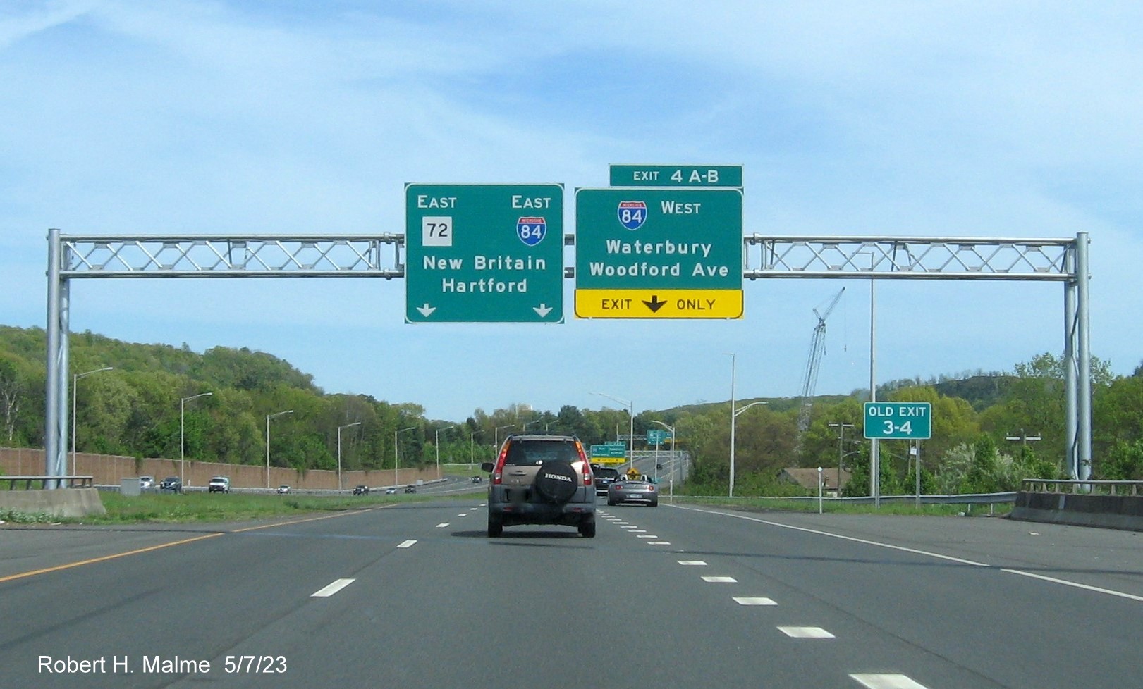 Image of 1/2 mile advance overhead sign for I-84 West/Woodford Avenue exits with new milepost based exit number and Old Exit 3-4 sign below on CT 72 East in Bristol, May 2023