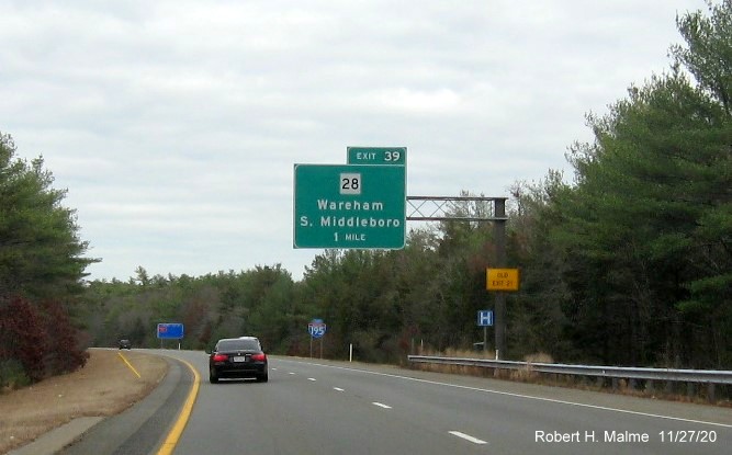 Image of 1-mile advance overhead sign form MA 28 exit with new milepost based exit number and yellow old exit number sign on support post on I-195 East in Wareham, November 2020