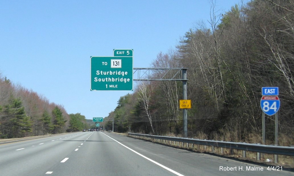 Image of 1 Mile advance overhead sign for To MA 131 exit with new milepost based exit number and yellow Old Exit 2 advisory sign on support on I-84 East in Sturbridge, April 2021