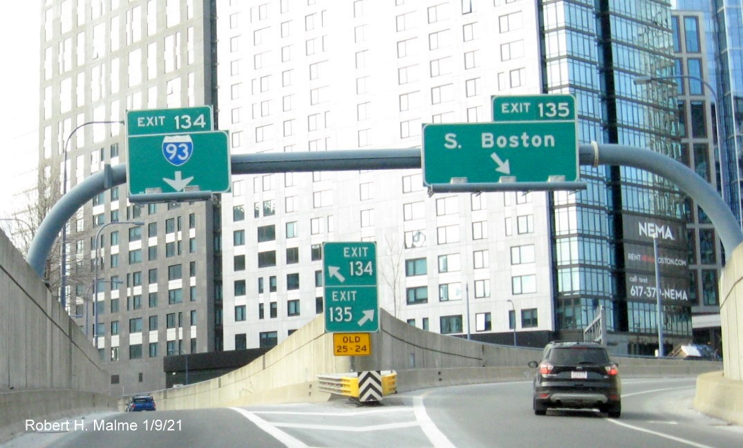 Image of overhead signs at split of I-93 and South Boston Exit ramps with new milepost based exit number and gore sign
                                       with yellow Old exit numbers sign below, January 2021