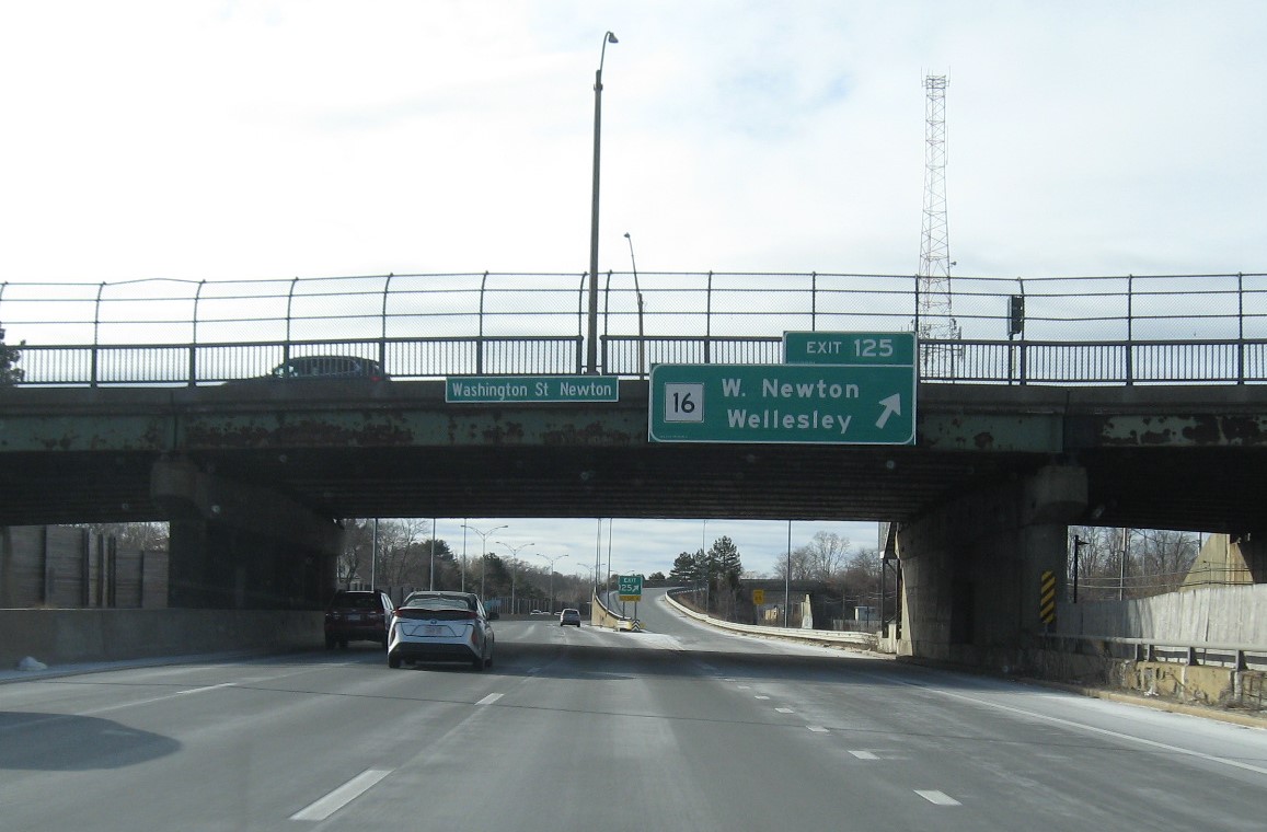 Image of overhead ramp sign for MA 16 Exit with new milepost based number and gore sign with new number and yellow old Exit 16 sign below on I-90 West in Newton, January 2021