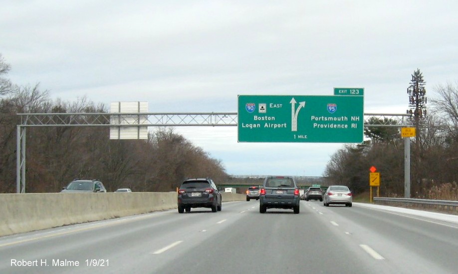Image of 1-Mile advance overhead diagrammatic sign for I-95 exit with new milepost based exit number and yellow Old Exit 14 sign on right support post on I-90/Mass Pike East in Weston, January 2021