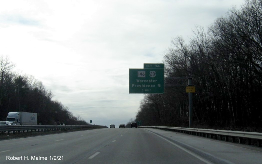 Image of 1-mile advance overhead sign for US 20/MA 146 exit with new milepost based exit number and yellow old exit sign on support post on I-90/Mass Pike West in Worcester, January 2021