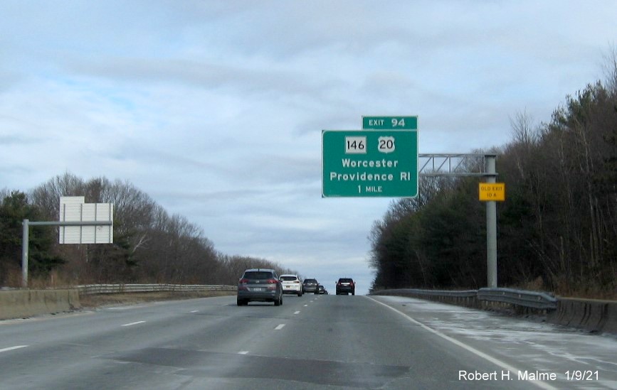 Image of 1-mile advance overhead sign for US 20/MA 146 exit with new milepost based exit number and yellow old exit sign on support post on I-90/Mass Pike East in Worcester, January 2021