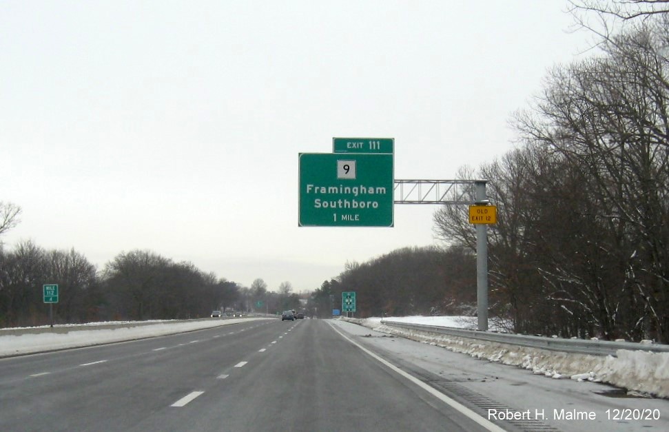 Image of 1-mile advance overhead sign for MA 9 exit with new milepost based exit number and yellow old exit number sign on support post on I-90/Mass Pike West in Framingham, December 2020