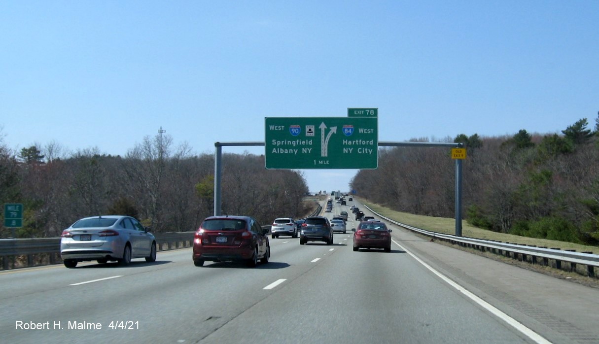 Image of 1 mile advance diagrammatic sign for I-84 exit with new milepost based exit number and yellow Old Exit 9 advisory sign on right support on I-90/Mass Pike West in Charlton, April 2021