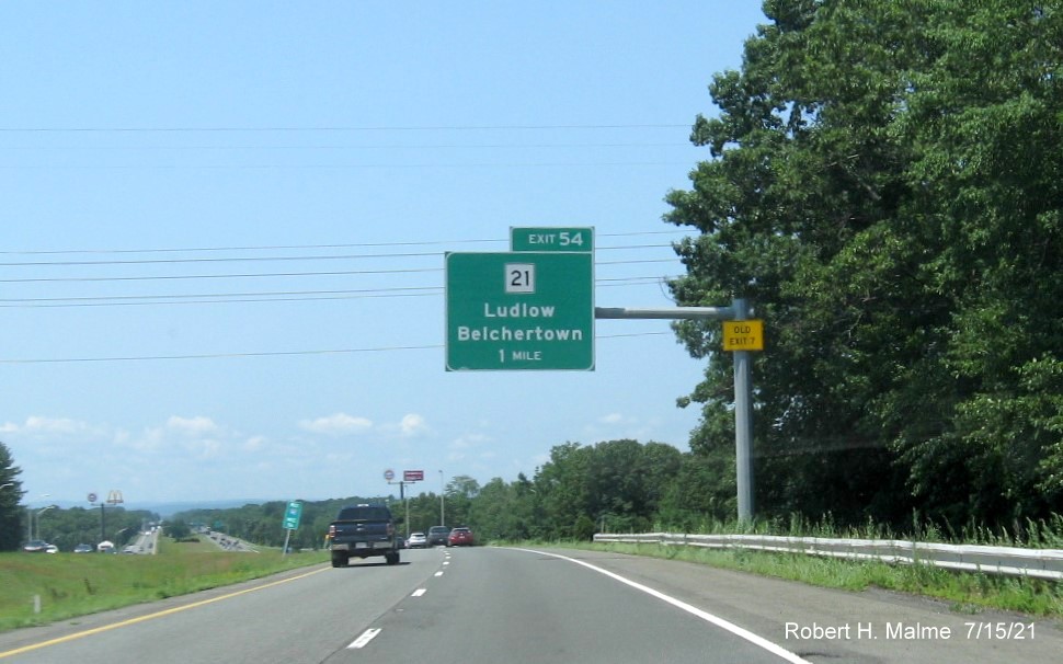 Image of 1 mile advance overhead sign for MA 21 exit with new milepost based exit number and yellow Old Exit 7 advisory sign on support on I-90/Mass Pike West in Ludlow, July 2021