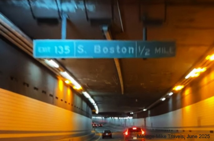 Image of 1/2 Mile advance overhead sign for South Boston exit in Fort Point Channel 
		Tunnel with milepost based exit number on I-90/Mass Pike East in Boston, screen grab from Mileage Mike Travels video, 
		June 2025