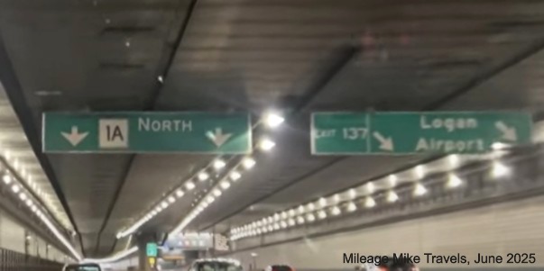 Image of overhead ramp sign connected to ceiling of the Ted Williams Tunnel with 
		new milepost based exit number for Logan Airport exit on I-90 East/Massachusetts Turnpike in East Boston, screen grab 
		from Mileage Mile video, June 2025
