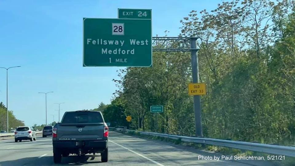 Image of 1 mile advance overhead sign for MA 28 Fellsway West exit with new milepost based exit number and yellow 
                                            Old Exit 33 advisory sign on support on I-93 South in Stoneham, May 2021