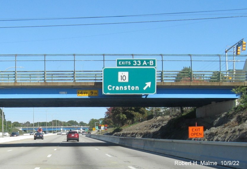Image of bridge mounted exit sign for RI 10 exit with new milepost based exit number and yellow Old Exit 16 sign on gantry arm on I-95 North in Cranston, October 2022