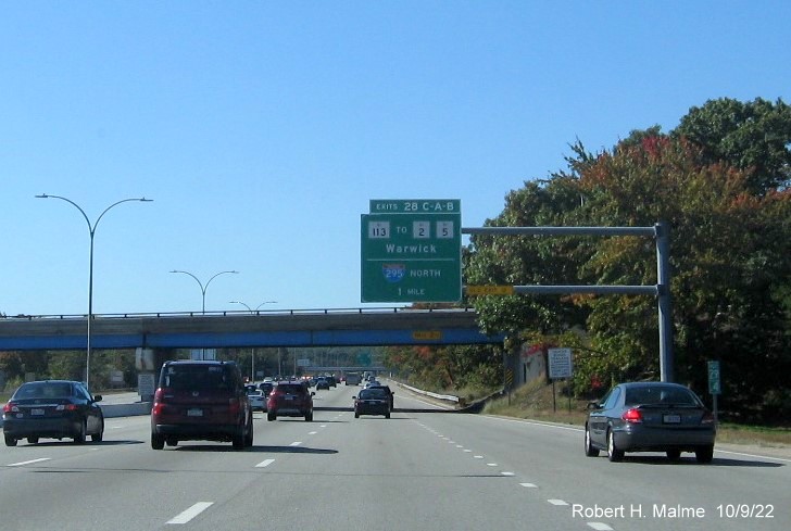 Image of 1 mile advance overhead sign for RI 113 and To I-295 North exits with new milepost based exit number and yellow Old Exits 12 B-A sign on gantry arm on I-95 South in Warwick, October 2022