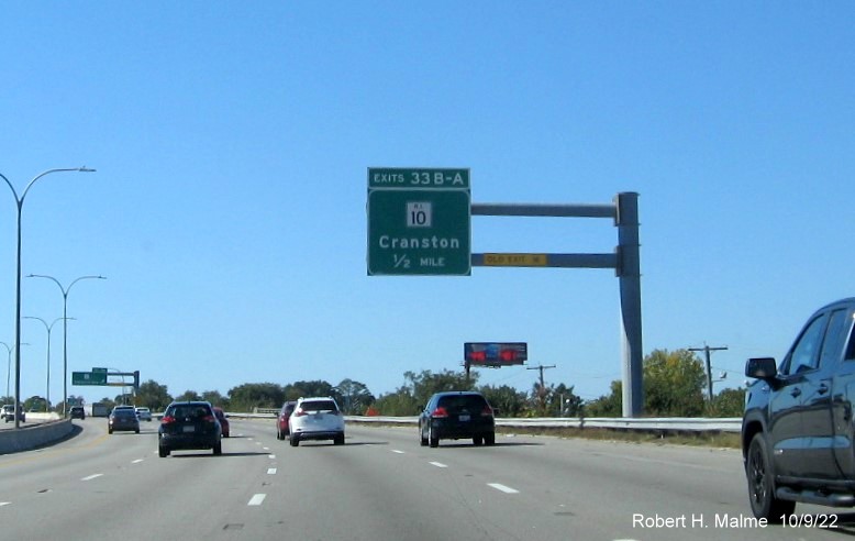 Image of overhead ramp sign for RI 10 exit with new milepost based exit number and yellow Old Exit 16 sign on gantry arm on I-95 South in Cranston, October 2022