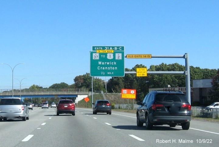Image of 1/2 mile advance overhead sign for RI 37 and Jefferson Blvd. exits with new milepost based exit numbers and yellow Old Exits 14-15 sign on gantry arm on I-95 North in Warwick, October 2022