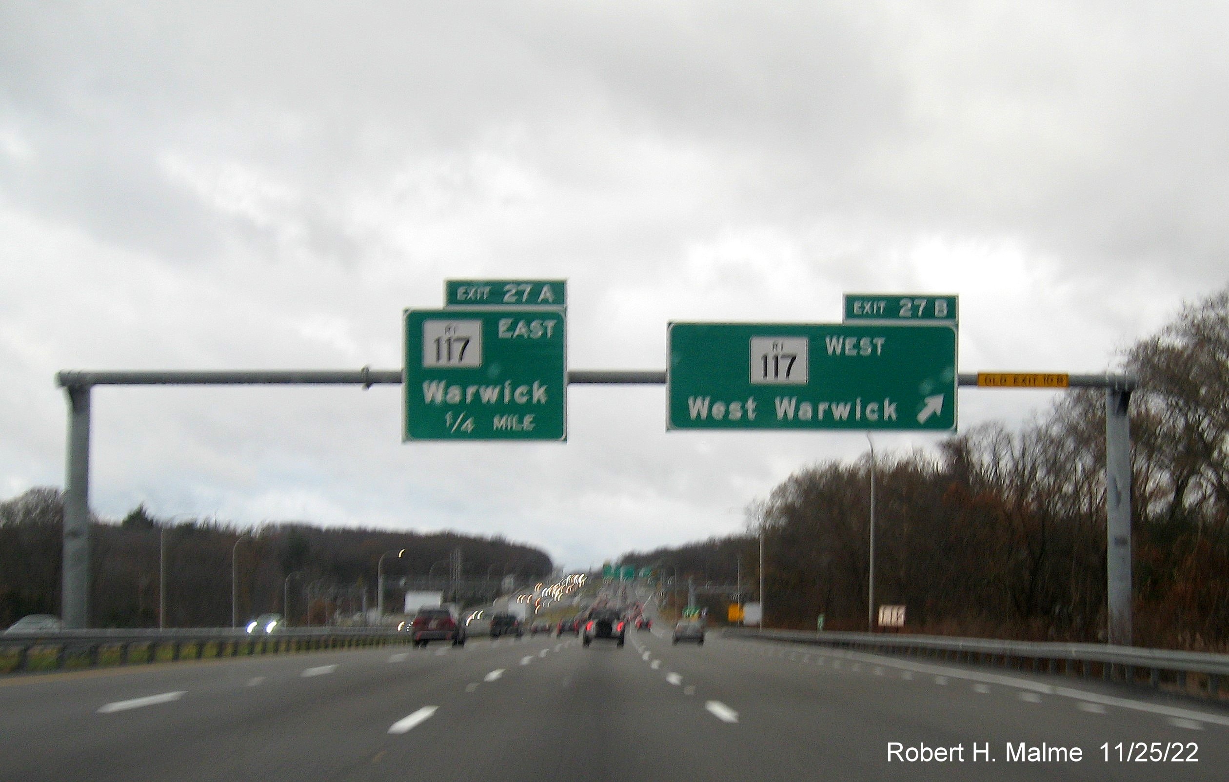 Image of overhead signs at ramp to RI 117 West exit with new milepost based exit numbers and yellow Old Exit 10B sign on right gantry arm on I-95 South in Warwick, November 2022