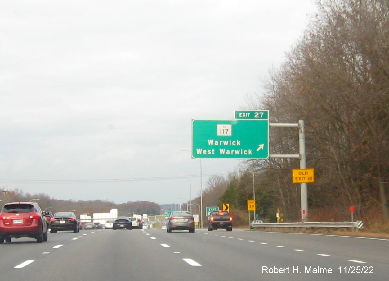 Image of overhead ramp sign for RI 117 exit with new milepost based exit number and yellow Old Exit 10 sign on gantry arm on I-95 North in West Warwick, November 2022