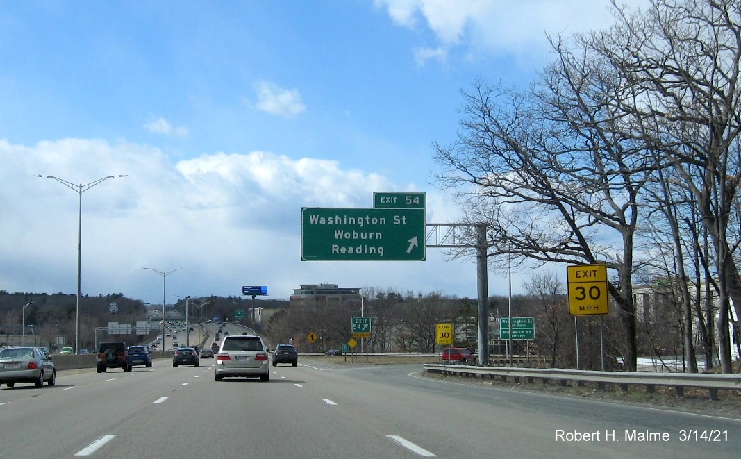 Image of overhead ramp sign for Washington Street exit with new milepost based exit number and gore sign in distance with new number and yellow Old Exit 36 sign below on I-95/MA 128 South in Woburn, March 2021