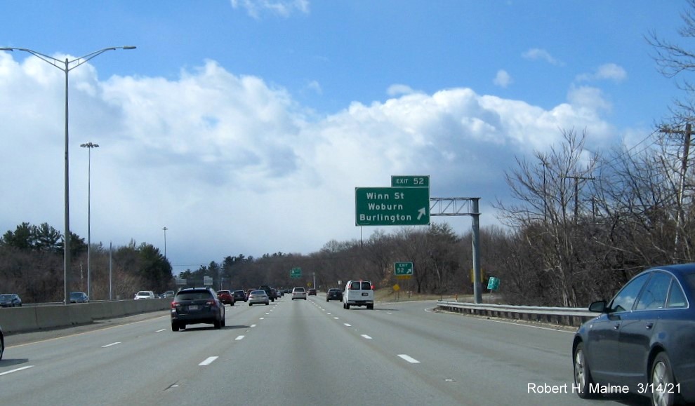 Image of overhead ramp sign for the Winn Street exit with new milepost based exit number gore sign in distance with new number and yellow Old Exit 34 advisory sign below on I-95/MA 128 South in Woburn, March 2021