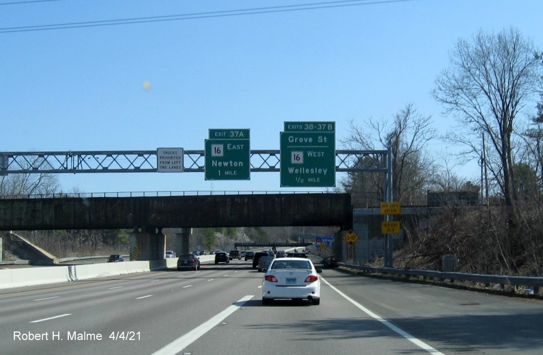 Image of overhead advance signs for MA 16 and Grove Street exits with new milepost based exit numbers and yellow Old Exits 22-21B and 21A advisory signs on right support on I-95/MA 128 South in Newton, April 2021