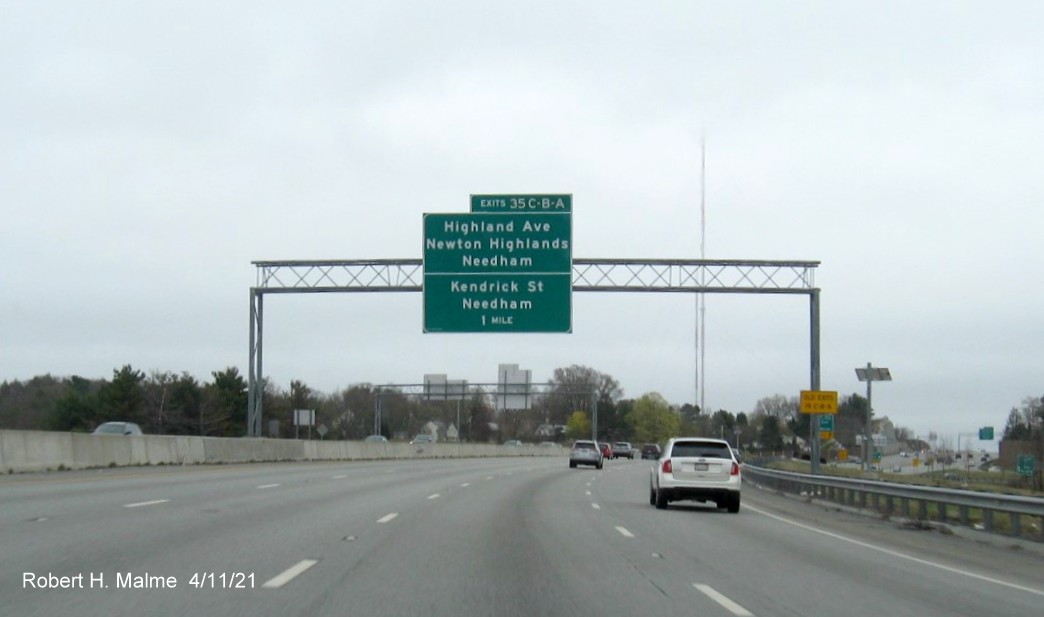 Image of 1 Mile advance overhead sign for Highland Avenue/Kendrick Street exits with new milepost based 
                                            exit numbers and yellow Old Exits 19 A-C advisory sign on right support on I-95/MA 128 South in Wellesley,                                             April 2021