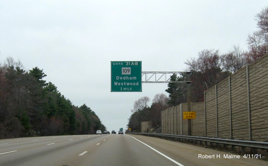Image of 1 Mile advance overhead sign for MA 109 exits with new milepost based exit numbers and yellow 
                                         Old Exits 16 A-B advisory sign on support on I-95/MA 128 North in Dedham, April 2021