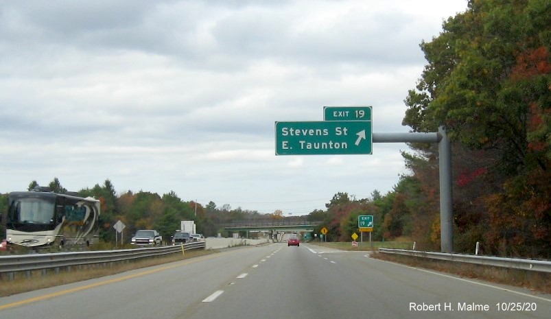 Image of overhead ramp sign and ground mounted gore sign for Stevens Street exit both with new milepost based exit numbers and yellow old exit number tab below gore sign on MA 140 North in Taunton, October 2020