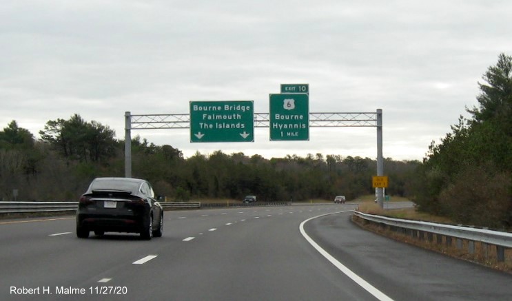 Image of 1 mile advance overhead sign for the US 6 exit with new milepost based exit number and yellow old exit sign on support post on MA 25 East in Bourne, November 2020