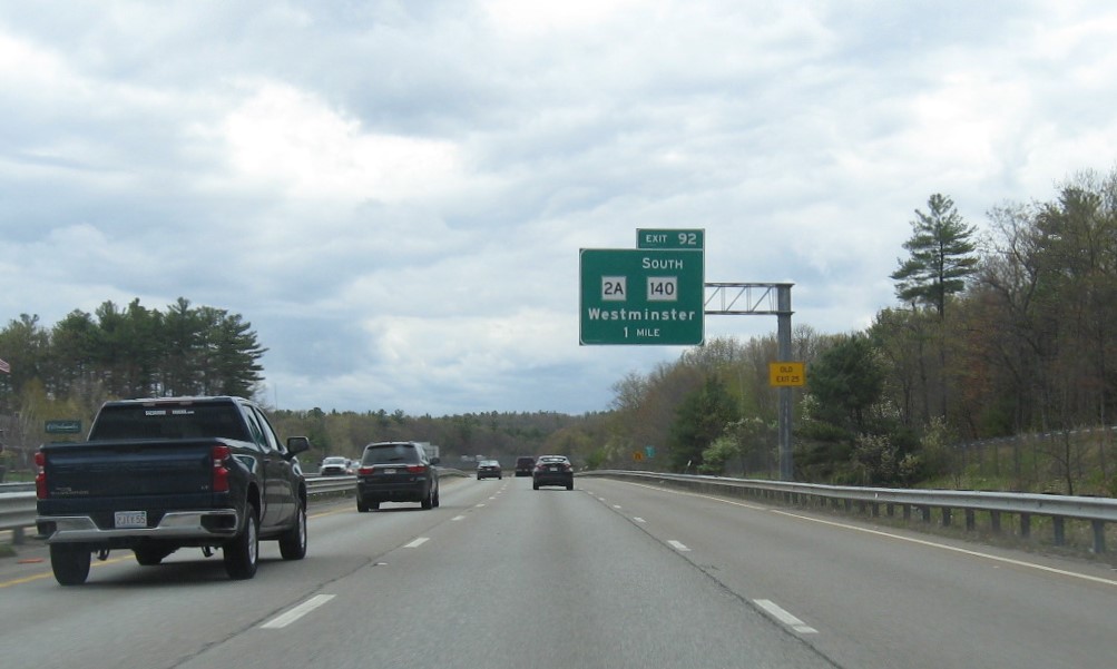 Image of 1 mile advance for MA 2A/South MA 140 exit with new milepost based exit number and yellow Old Exit 25 advisory sign on support on MA 2 West in Westminster, May 2021