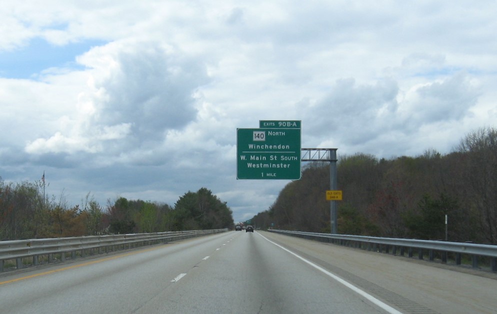 Image of 1 mile advance overhead sign for MA 140 North/West Main Street exits with new milepost based exit numbers and yellow Old Exits 24 B-A advisory sign on support on MA 2 West in Westminster, May 2021