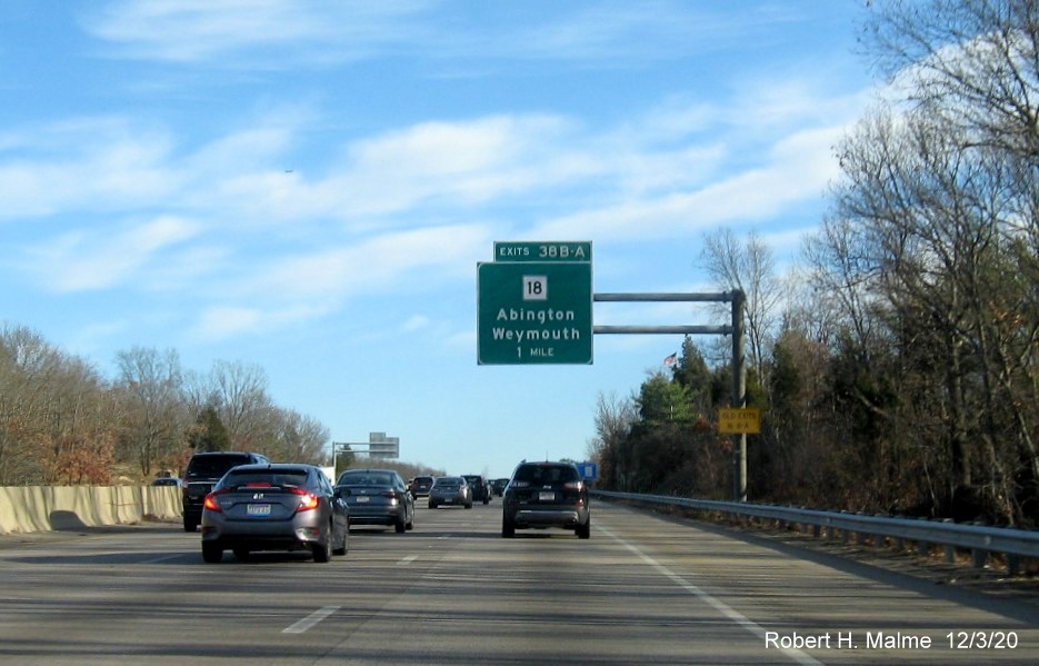 Image of 1-Mile advance overhead sign for MA 18 exits with new milepost based exit number and yellow old exit number sign on support on MA 3 South in Weymouth, December 2020