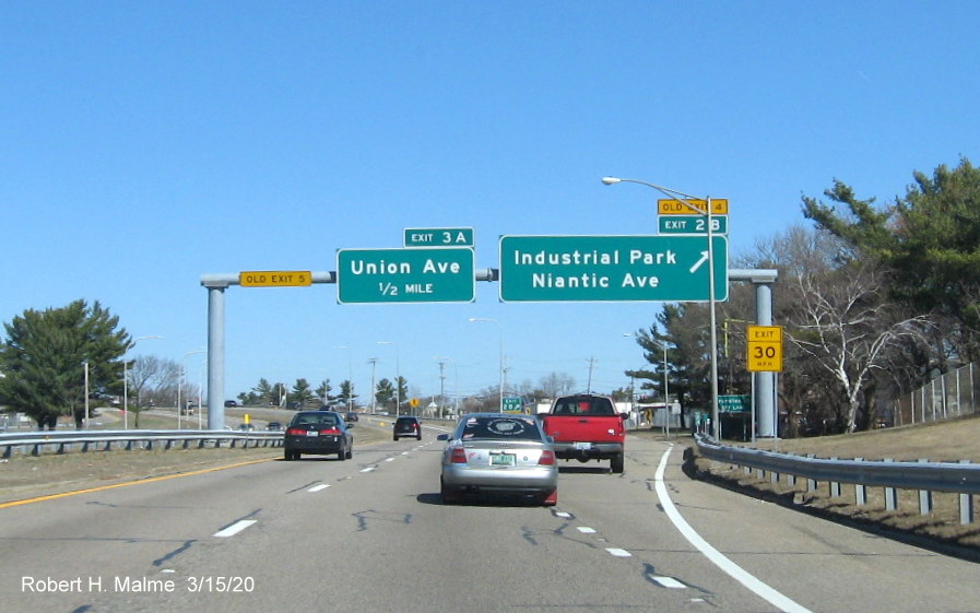Image of overhead signage at ramp to the Industrial Park/Niantic Avenue exit on RI 10 North in Providence with new exit numbers and old exit number tabs, one mounted to the side gantry post, taken in March 2020