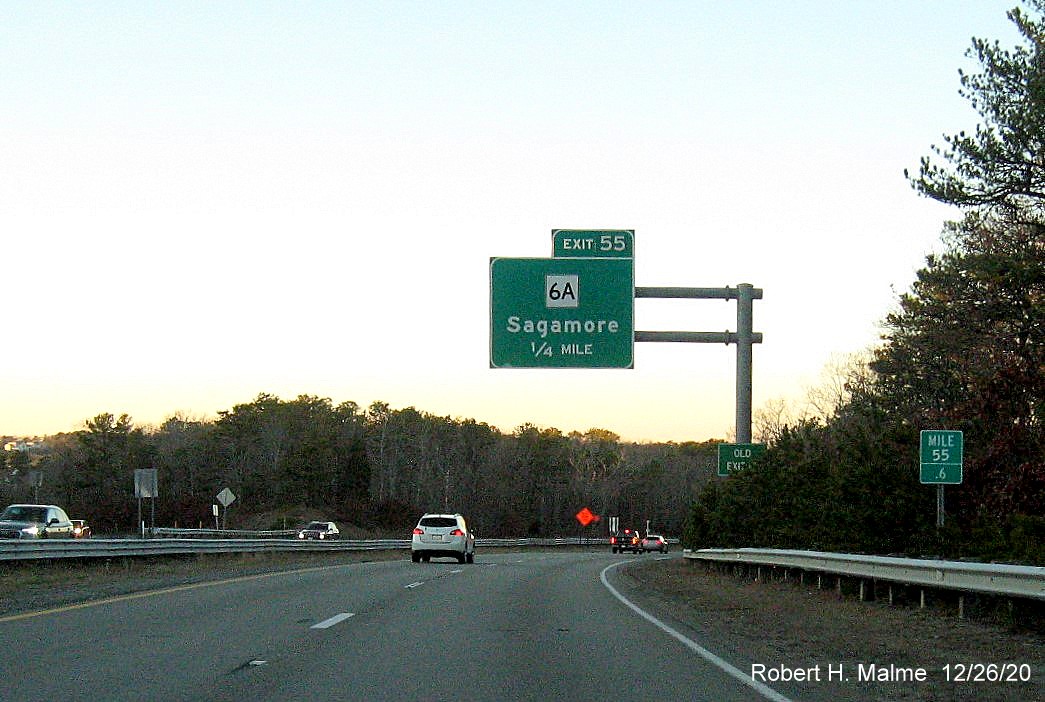 Image of 1/4 mile advavnce overhead sign for MA 6A exit with new milepost based exit number and green old exit sign on support post on US 6 West in Bourne, December 2020
