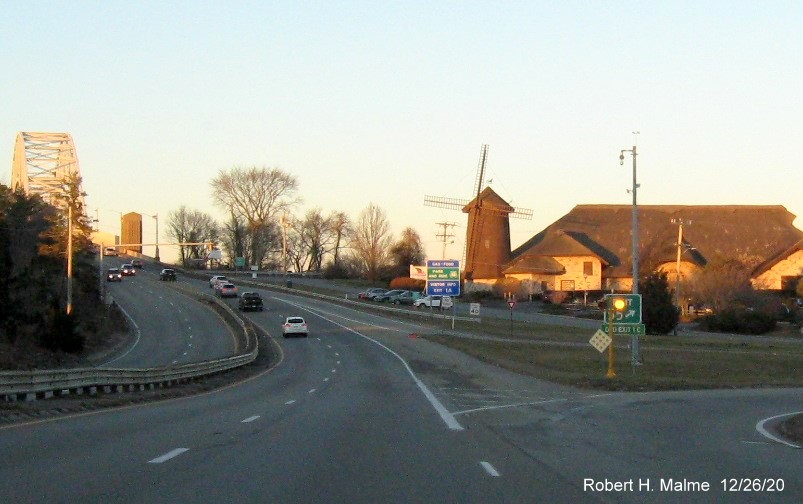 Image of gore sign for MA 6A exit with new milepost based exit number and green old exit sign below (obstructed by flashing light) on US 6 West in Bourne, December 2020