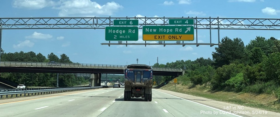 Image of overhead signs for Hodge Road and New Hope Road exits on I-87 North/US 64/264 East with new I-87 exit number tabs, by David Johnson
