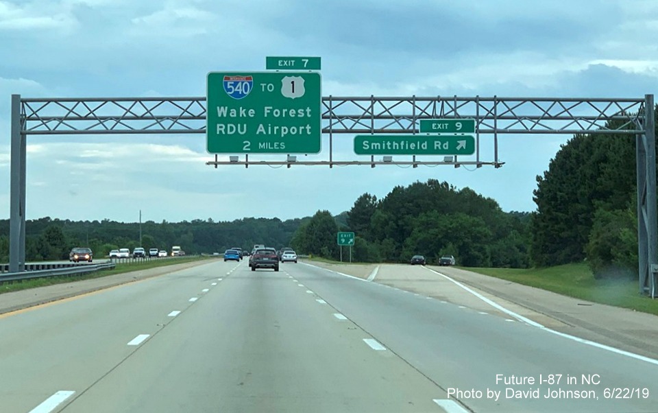 Image of overhead signs with new I-87 exit number tabs at ramp to Smithfield Road on I-87 South, US 64/264 West in Knightdale, by David Johnson