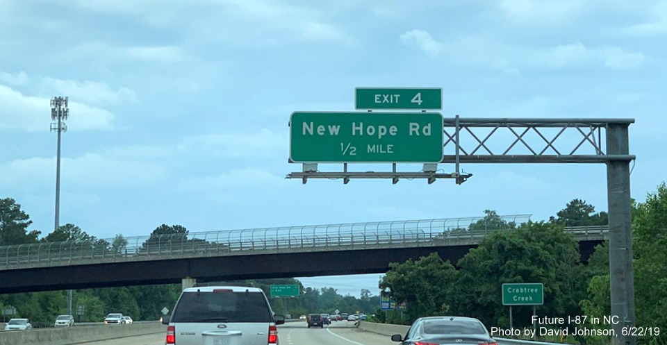 Image of overhead 1/2 mile advance sign for New Hope Road exit with new I-87 exit number tab on I-87 South, US 64/264 West in Raleigh